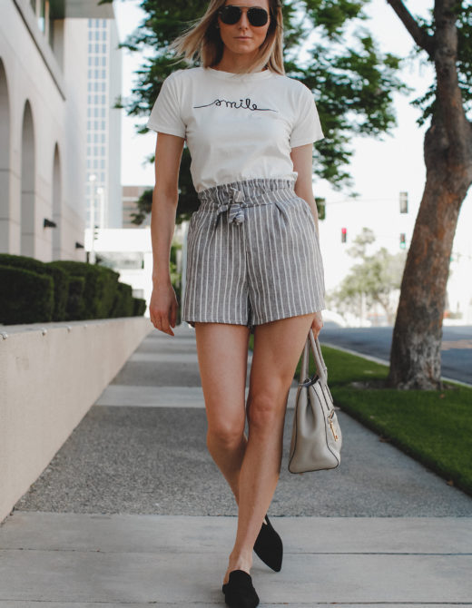 Paper bag shorts trend featured by top US fashion blog, Tea Cups & Tulips: image of a woman wearing Light grey paper bag shorts and a smile tee