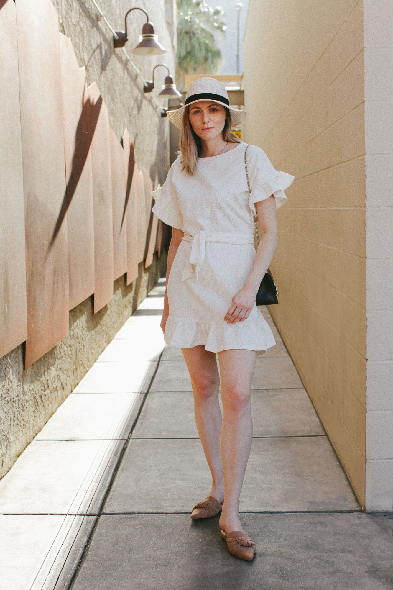 Cute summer ruffle dress styled by top US fashion blog, Tea Cups & Tulips: image of a woman wearing an H&M cream ruffle dress, Furla crossbody bag, H&M mules, ASOS hat and Amazon pearl hair clip.