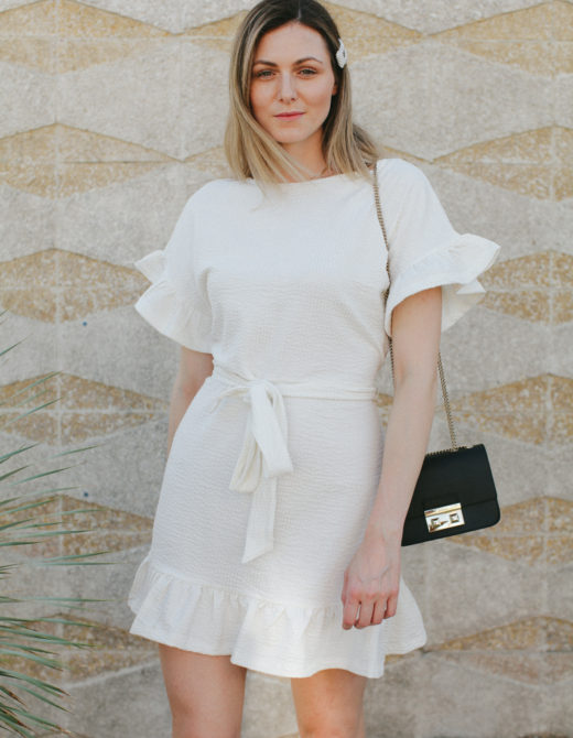 Cute summer ruffle dress styled by top US fashion blog, Tea Cups & Tulips: image of a woman wearing an H&M cream ruffle dress, Furla crossbody bag, H&M mules, ASOS hat and Amazon pearl hair clip.